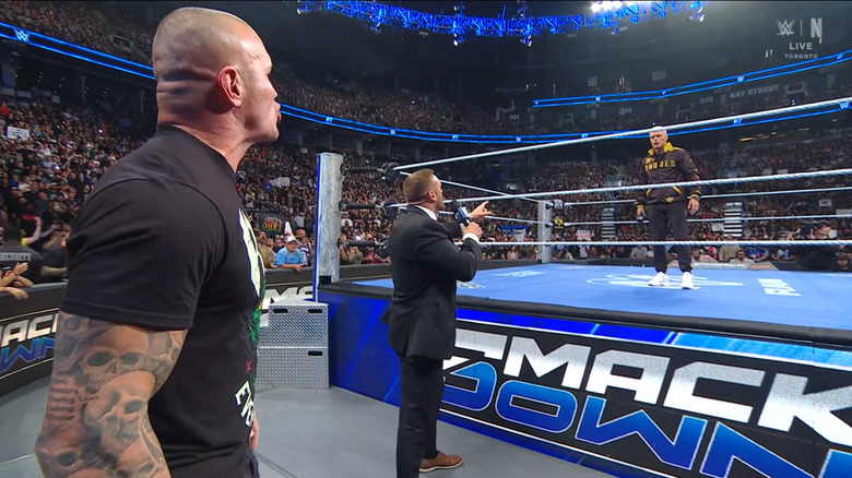 Orton and Rhodes staring down one another in the ring as Aldis stands between them