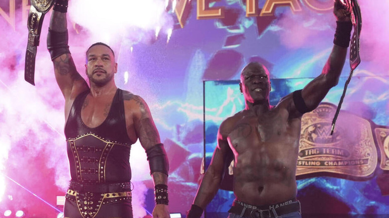 Damian Priest and R-Truth hoist up the WWE Tag Team Championships.