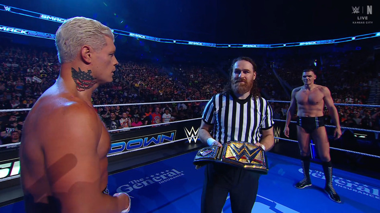 Rhodes y Gunther se miran fijamente en el ring mientras Zayn se interpone entre ellos.