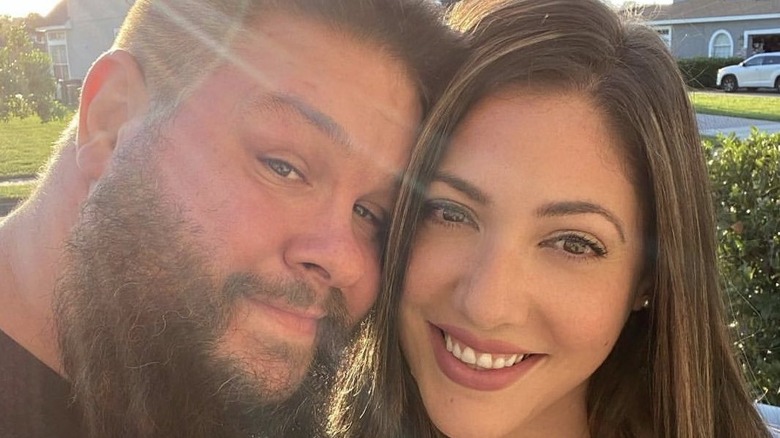 Kevin Owens and his wife, Karina, pose smiling for the camera on a sunny day in a selfie posted to his X account.