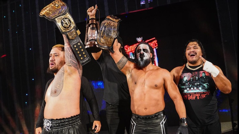 Solo Sikoa and Tama Tonga, flanked by JC Matteo, Talla Tonga, and Tonga Loa, hold up their newly-won WWE Tag Team Championships on the stage on 