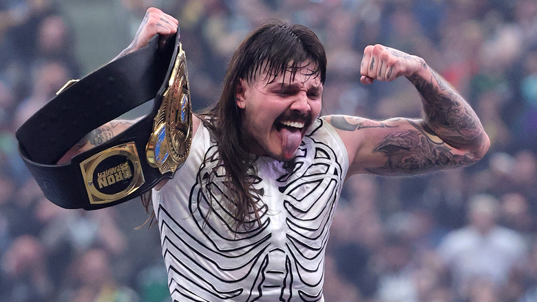 Dominik Mysterio flexing and sticking his tongue out while holding the WWE Intercontinental Championship