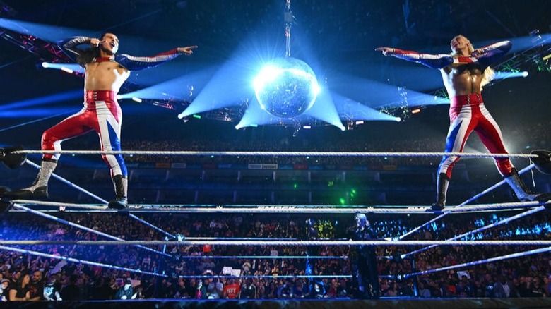 Pretty Deadly ( Kit Wilson and Elton Prince) point at each other and smile as a shiny disco ball accompanies them in the middle of the ring