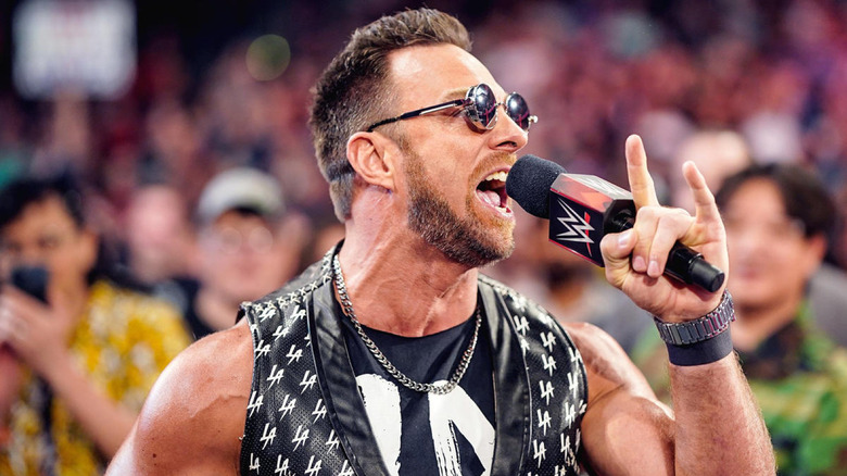 Wrestler LA Knight wearing sunglasses, speaking into a WWE microphone