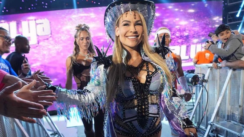 Natalya smiles to the crowd as she heads to the ring, flanked by Maxxine and Akira Tozawa, for a match on 