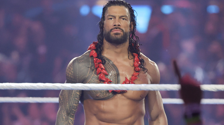 Roman Reigns stands stone-faced amidst a crowd of fans acknowledging him.