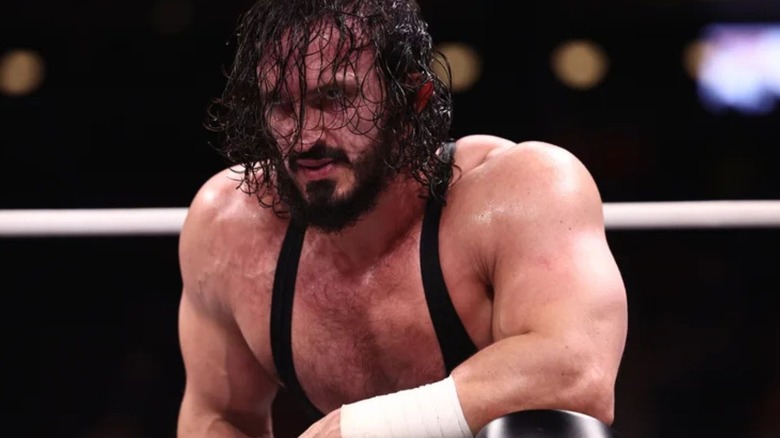 Pac kneels in the ring, hair in front of his face, after a match on AEW programming.