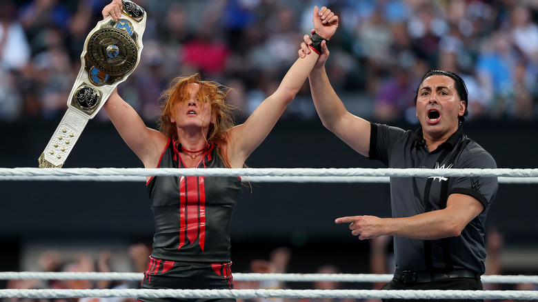 Becky Lynch holds the Women's Intercontinental Championship in one hand as her other hand is raised by the referee.