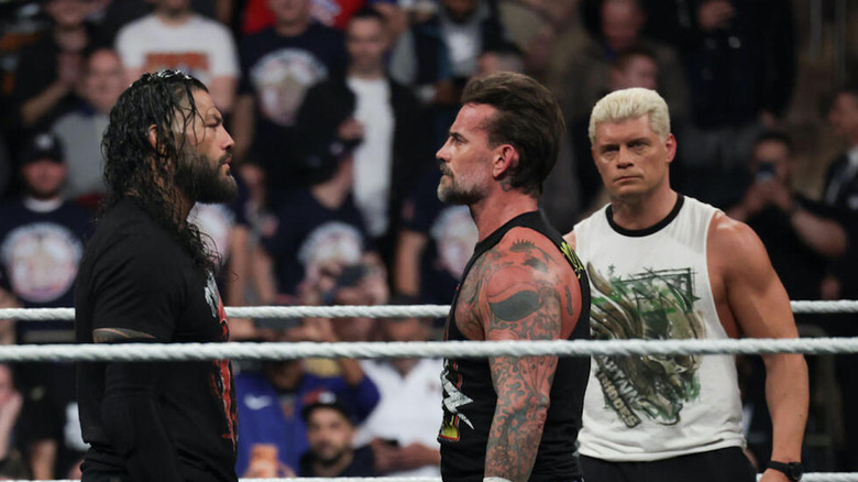 Roman Reigns staring down CM Punk with Cody Rhodes looking on