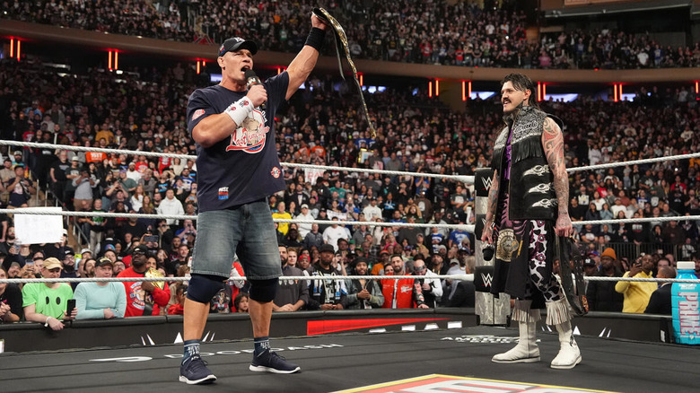 John Cena holds up the Intercontinental title while speaking with Dominik Mysterio