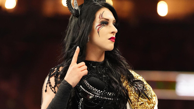 Stephanie Vaquer looks on dominantly as she holds her WWE Women's World Championship, with a one pointed up on her fingers.
