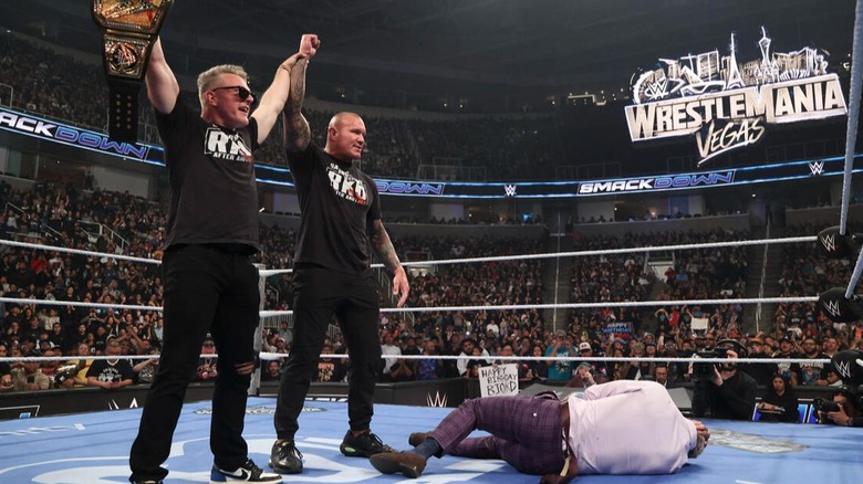 Pat McAfee (holding the Undisputed WWE Championship) and Randy Orton stand tall over a fallen Cody Rhodes during an episode of 