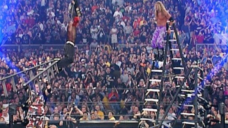 Edge, who stands on a ladder, looks to spear Jeff Hardy, hanging by the title belts in the middle of the ring, during TLC 2 at WrestleMania X-Seven.