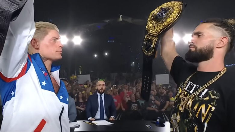 Cody Rhodes holds the Undisputed WWE Championship in front of Seth "Freakin'" Rollins, who is hoisting up the World Heavyweight Championship.