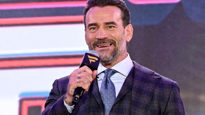 CM Punk is holding a microphone and smiling