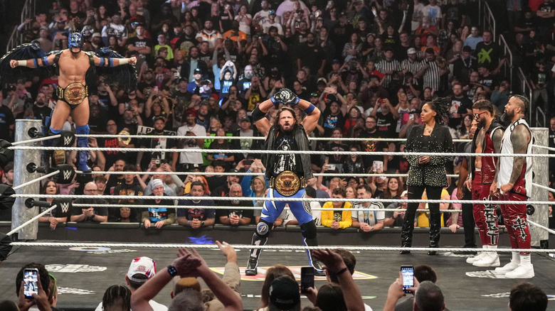 Dragon Lee and AJ Styles posing in the ring while the Usos look on