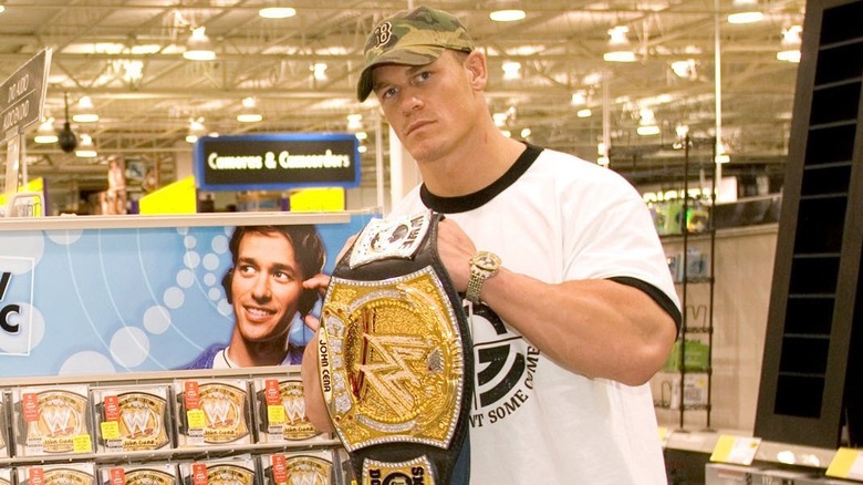 John Cena with his spinner WWE Championship next to a rack of his CDs