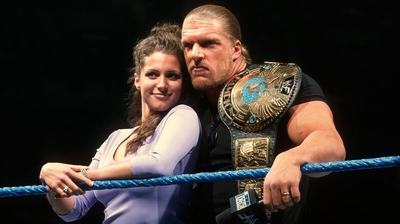 Stephanie McMahon and Triple H posing together in the ring while HHH has the WWF Championship over his shoulders.