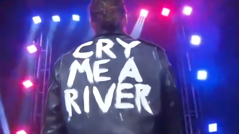 Jack Perry stands with his back facing the camera. On the back of his leather jacket are the words "cry me a river" painted in white.